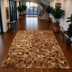 Op de afbeelding: Een rechthoekig vloerkleed met een geometrisch patroon bestaande uit gestikte lederen tegels in verschillende tinten bruin, beige en crème. Het kleed vertoont een herhalend achthoekig en vierkant motief over het gehele, platliggende oppervlak.