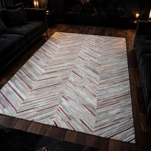 May include: A rectangular area rug featuring a chevron pattern composed of thin, horizontal strips in shades of white, gray, and brown, accented with intermittent, vibrant red lines throughout the textured surface of the floor covering.