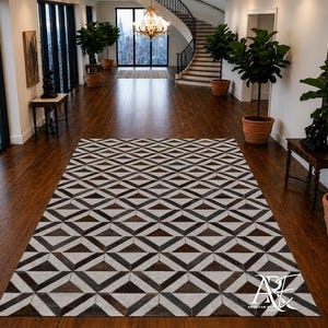 Op de afbeelding: Een rechthoekig vloerkleed met een herhalend geometrisch patroon van donkerbruine en lichtgrijze driehoeken. Het kleed ligt plat op een donkere houten vloer in een grote kamer met hoge ramen en kamerplanten in potten.