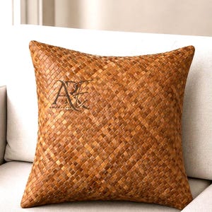 May include: A square throw pillow featuring a woven brown leather-like texture with a grid pattern. The surface displays a dark logo watermark with the text AMERICAN RUG DEPO in the upper left quadrant of the pillow cover, showing a consistent weave.