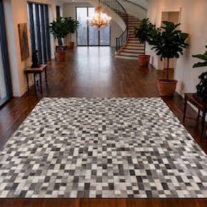 Può includere: Un tappeto rettangolare caratterizzato da un motivo a mosaico composto da piccole tessere quadrate in varie tonalità di grigio, nero e bianco. Il tappeto è formato da numerosi pezzi singoli disposti in una struttura a griglia.