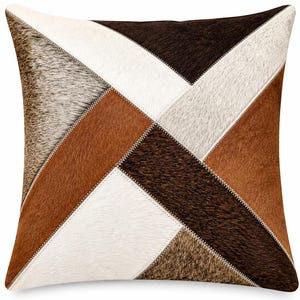 May include: Square decorative pillow with a patchwork design. The pillow features geometric shapes in shades of brown, white, and gray, with visible stitching. The pillow is made of a soft, textured material, adding a rustic touch to home decor.