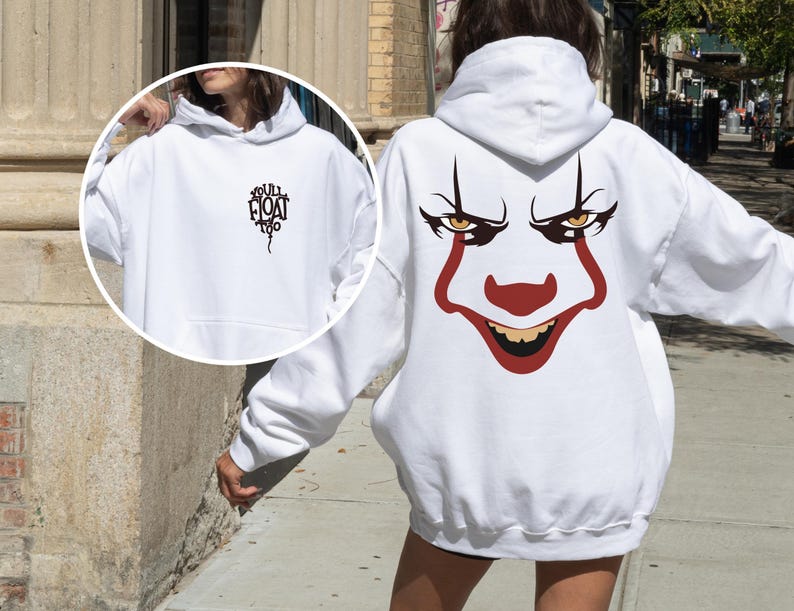 May include: A white hooded sweatshirt featuring a large graphic of a clown face on the back with red and black details. The front chest area displays a small black graphic of a balloon with the text "YOU'LL FLOAT TOO" printed in a stylized font.