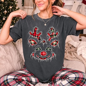 May include: A charcoal gray short-sleeve t-shirt featuring a distressed-style graphic of a reindeer face. The reindeer design is filled with a red, green, and white plaid pattern, with frayed edges around the antlers, ears, and nose.