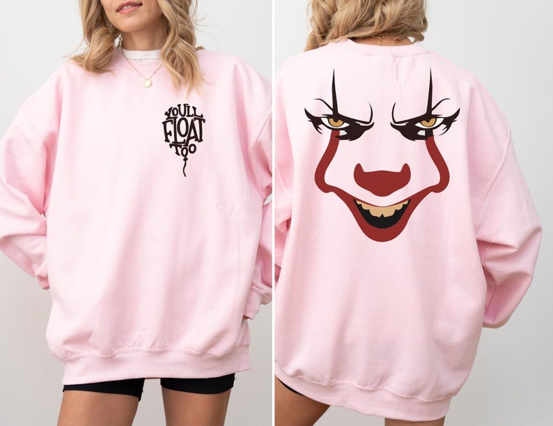 May include: A light pink crewneck sweatshirt featuring a black graphic on the front left chest that reads "YOU'LL FLOAT TOO" inside a balloon shape. The back of the sweatshirt displays a large, detailed graphic of a clown face with red makeup.