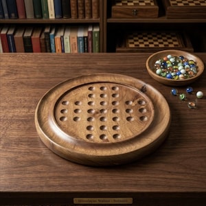 May include: A round wooden solitaire game board made of Himalayan walnut with a cross-shaped pattern of thirty-three circular indentations. A small wooden bowl filled with colorful glass marbles sits nearby, with a few loose marbles on the table.