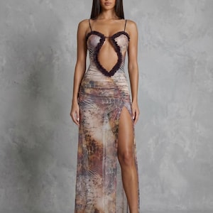 Op de afbeelding: Een vloerlange mouwloze jurk met een transparante mesh overlay met een bruine en beige dierenprint en schriftpatroon. Het lijfje heeft een grote druppelvormige uitsnijding afgezet met donkerbruine ruches en dunne spaghettibandjes.