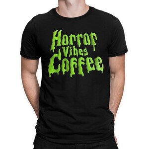 May include: A black short-sleeved t-shirt featuring the text "Horror Vibes Coffee" printed in a bright lime green, dripping, slime-like font across the chest. The garment has a standard crew neckline and a solid black background color.