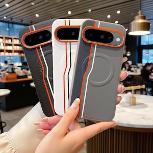 May include: Three smartphone cases in black, white, and gray, each featuring a textured finish, a prominent orange camera module surround, and vertical racing-style stripes in orange and white running down the back of the protective covers.