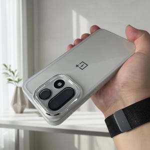 May include: A clear, transparent protective phone case for a OnePlus smartphone. The case features a precise cutout for the rear camera module, which contains three circular lenses and a rectangular sensor, and displays the OnePlus logo.