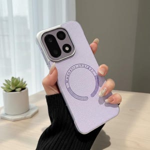 May include: A light purple smartphone case with a textured finish and a dark purple circular magnetic charger ring printed on the back. The case features a raised camera cutout area with three circular lens openings and a silver-toned border.