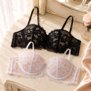 May include: Two bras are shown, one black and one blush pink. The black bra has detailed lace and black straps. The blush pink bra features white lace and straps. Both bras are displayed on a light-coloured surface.