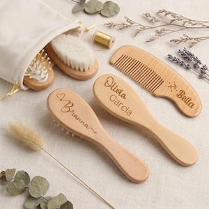 May include: A set of light-colored wooden hair brushes and a comb, featuring engraved names including Brianna, Olivia Garcia, and Bella. The items are arranged with a soft fabric pouch and a small spool of gold thread on a neutral textile surface.