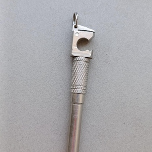 Puede incluir: Un colgante multiherramienta de metal plateado que presenta una cabeza de abridor de botellas con un pequeño grabado de estrella, una sección de agarre moleteada texturizada y una base cilíndrica lisa. Incluye una anilla metálica superior.