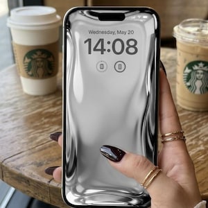 Könnte beinhalten: Ein Smartphone mit schwarzem Rahmen zeigt ein flüssiges, silbernes Metallic-Hintergrundbild, die Uhrzeit 14:08 Uhr und das Datum Mittwoch, 20. Mai. Der Bildschirm enthält zwei kreisförmige Symbole in der Mitte und eine Statusleiste oben.