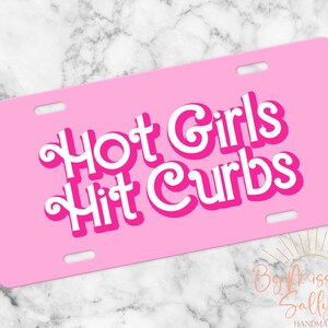 May include: A pink license plate with the text "Hot Girls Hit Curbs" in white, outlined in a darker pink. The plate has four mounting holes and a rounded rectangular shape. The background is a marble pattern.