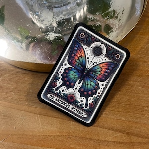 May include: A black and white tarot card with a colorful butterfly illustration. The card reads "The Antisocial Butterfly".