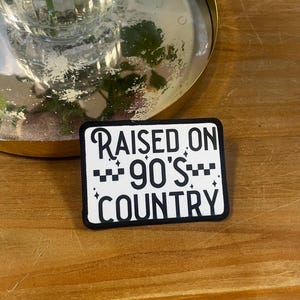 May include: Black and white iron-on patch with the text "RAISED ON 90'S COUNTRY" in a white font on a black background.