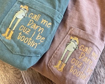May include: Two long-sleeved shirts, one teal and one mauve, each featuring a pocket with an embroidered frog wearing a cowboy hat and boots. The text "call me Darn cuz I be tootin'" is embroidered on the pocket.