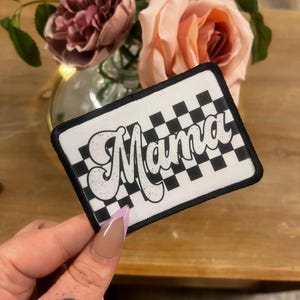 May include: Black and white checkered fabric patch with the word "Mama" in a white retro font.
