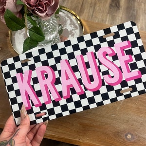 May include: A black and white checkered license plate with the name "KRAUSE" in pink letters.