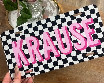 Puede incluir: Una placa de matrícula a cuadros negros y blancos con el nombre "KRAUSE" en letras rosas.