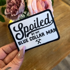 May include: White patch with black border and text that reads "Spoiled by my Blue Collar Man" with a black pickaxe symbol.