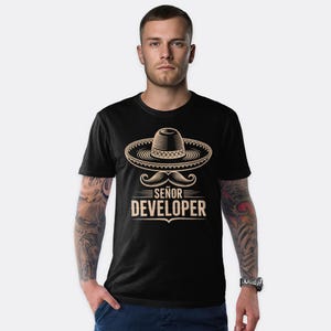 May include: Black t-shirt with a sombrero and mustache graphic. The text reads "Señor Developer" in a stylized font. The design is in shades of tan and brown.