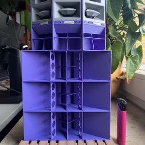 May include: A purple 3D-printed speaker array model featuring the text FUNKT ONE on the upper sections. The structure is composed of multiple square horn compartments and sits on two brown miniature pallets next to a pink lighter.