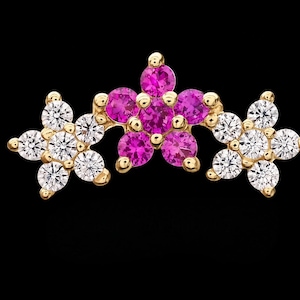 May include: A gold jewelry piece featuring three flower-shaped clusters. The central flower is composed of five round pink gemstones, while the two flanking flowers are each composed of five round clear white gemstones set in yellow gold.