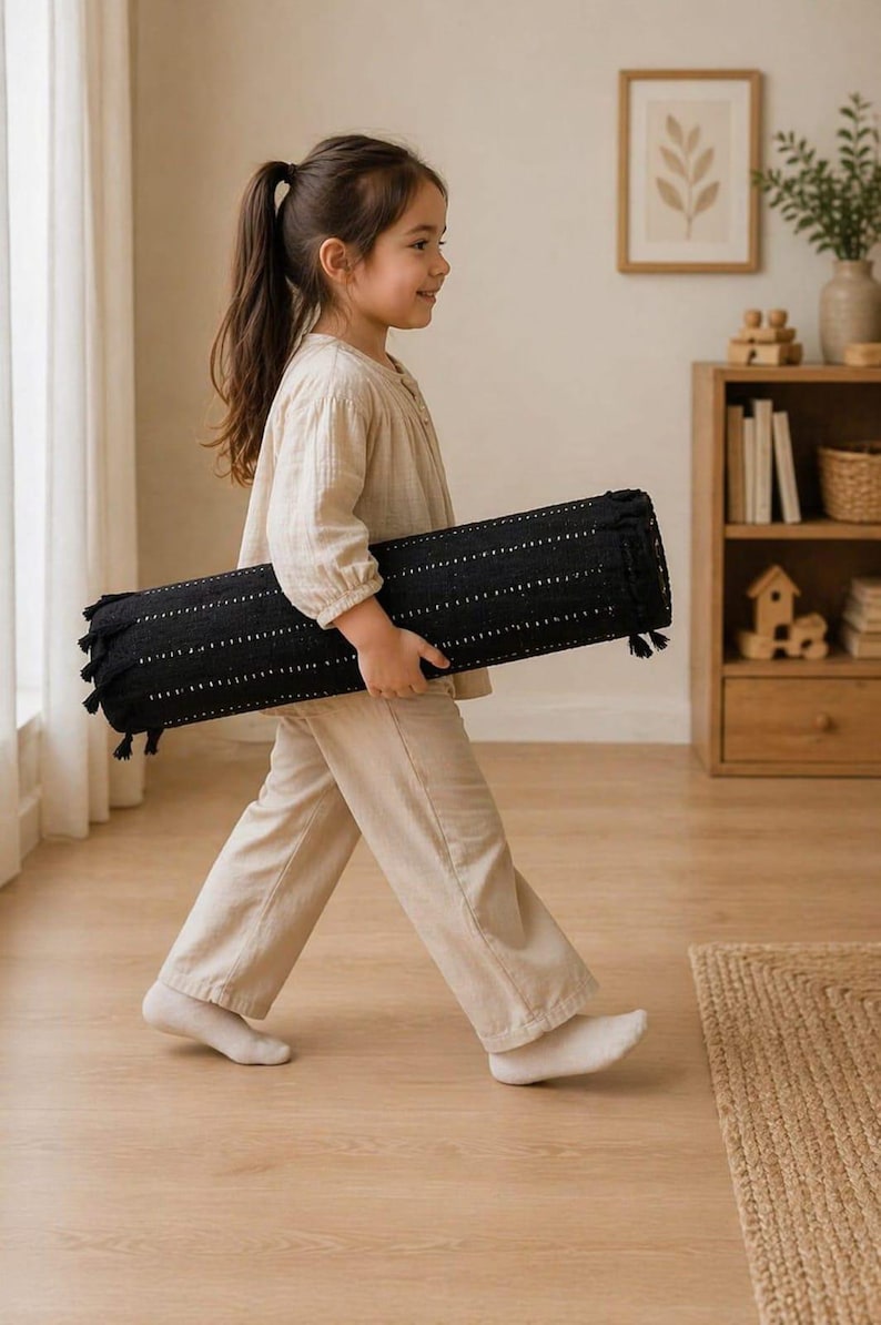 May include: A black cylindrical bolster pillow featuring a textured fabric with small white dotted patterns and decorative tassels on both ends. The pillow is held horizontally, showcasing its elongated shape and detailed woven construction.