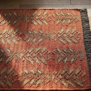 Könnte beinhalten: Terracottafarbener Teppich mit einem sich wiederholenden Blattmuster in Beige und Braun. Der Teppich hat eine strukturierte Oberfläche und einen Fransenrand. Dieser dekorative Teppich eignet sich für Wohnzimmer, Schlafzimmer oder Eingangsbereiche.