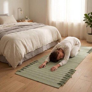 May include: A rectangular sage green rug featuring a textured ribbed pattern and decorative fringe along the shorter edges. The rug is crafted from a soft, woven material and is positioned flat on a light-colored wooden floor surface.