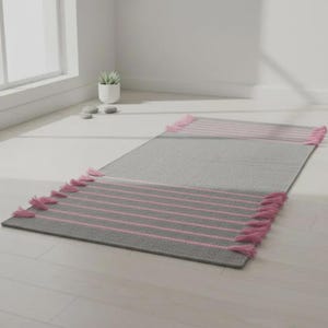 May include: A rectangular area rug featuring a solid gray center with horizontal pink stripes at both ends. The rug is finished with pink tassels along the short edges, creating a textured border that contrasts with the smooth gray fabric.