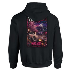 May include: Black hooded sweatshirt featuring a vibrant graphic of a car driving on a road with Japanese text and imagery. The design includes a mountain, cherry blossoms, and road signs. The text "Legend Never Die" is also visible.