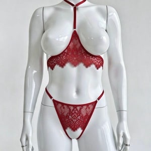 May include: A red lace lingerie set consisting of a bralette and matching thong. The bralette features a scalloped edge, a vertical strap connecting to a choker-style neck band, and thin straps. The thong has a matching lace front panel.