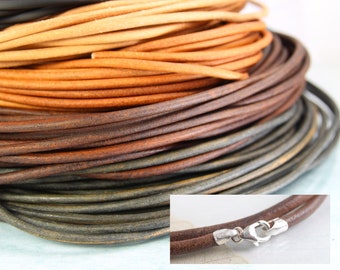 May include: A close-up of a stack of different colored leather cords. The cords are arranged in a spiral pattern, with the darkest cord at the bottom and the lightest cord at the top. A silver clasp is visible in the lower right corner of the image.