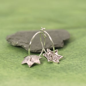 May include: A pair of silver hoop earrings with a star-shaped design. The stars have a detailed, intricate pattern.