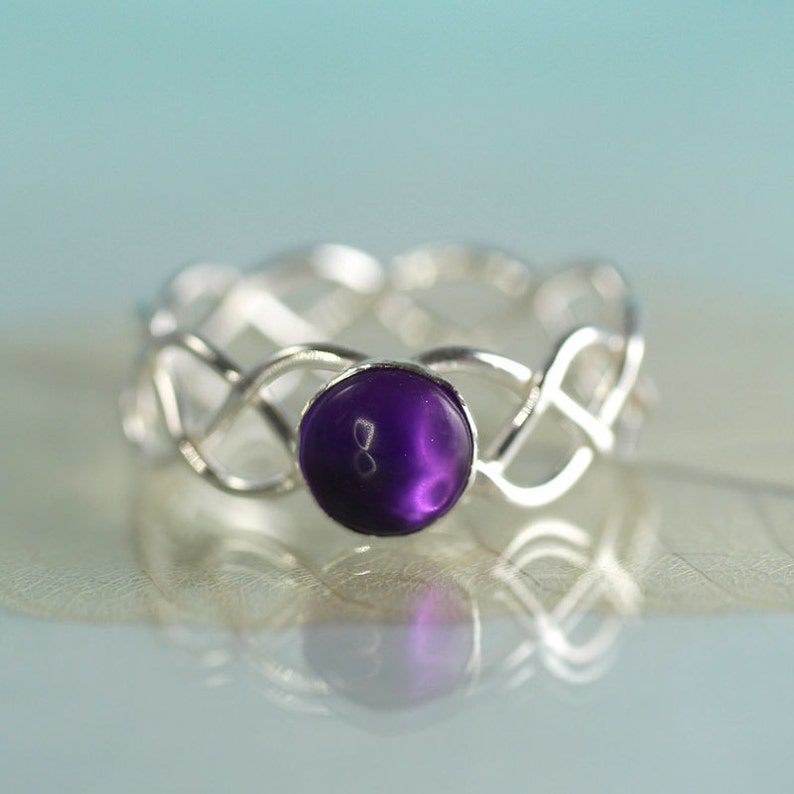 May include: A silver ring with a purple gemstone set in a woven band.