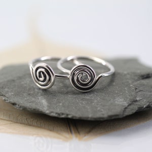Peut inclure: Deux bagues en argent avec un motif en spirale. Les bagues sont empilées l'une sur l'autre.