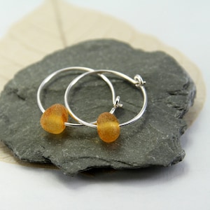 Pode incluir: Um par de brincos de argola de prata com uma pequena conta redonda de cor âmbar em cada argola.