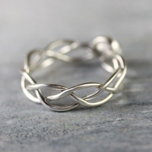 May include: A silver braided ring with a woven design. The ring is made from a single piece of metal that is twisted and intertwined to create a unique and intricate pattern.