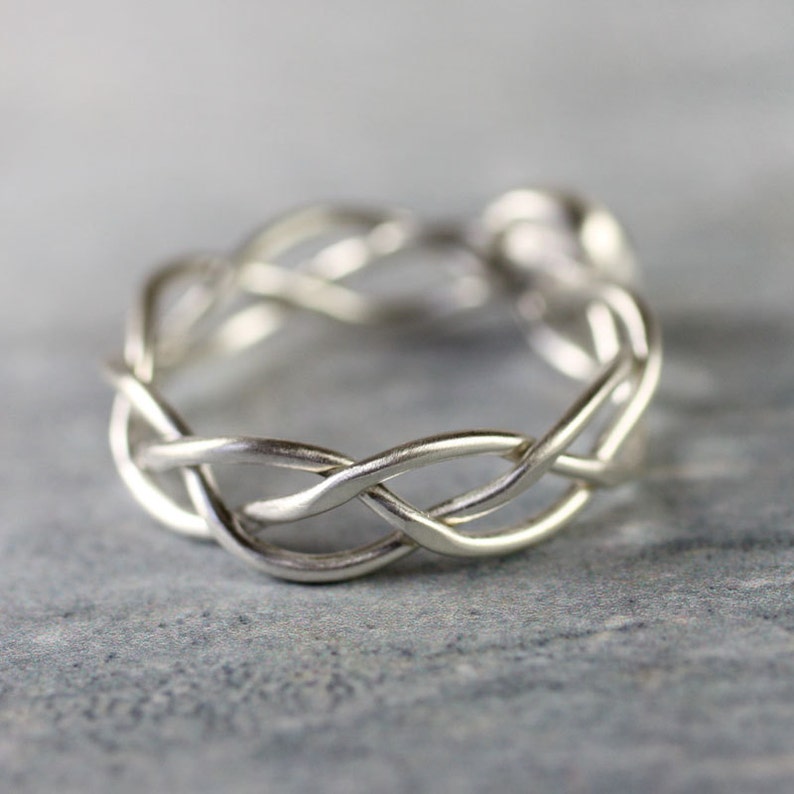 May include: A silver braided ring with a woven design. The ring is made from a single piece of metal that is twisted and intertwined to create a unique and intricate pattern.