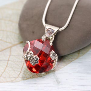 Peut inclure: Un collier avec un pendentif rouge en forme de cœur facetté et des détails en métal argenté. Le pendentif est suspendu à une fine chaîne argentée. Le travail du métal présente des motifs floraux et de vigne, ajoutant une touche d'élégance.
