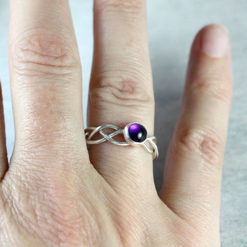 May include: A silver ring with a braided band and a purple gemstone in the centre.