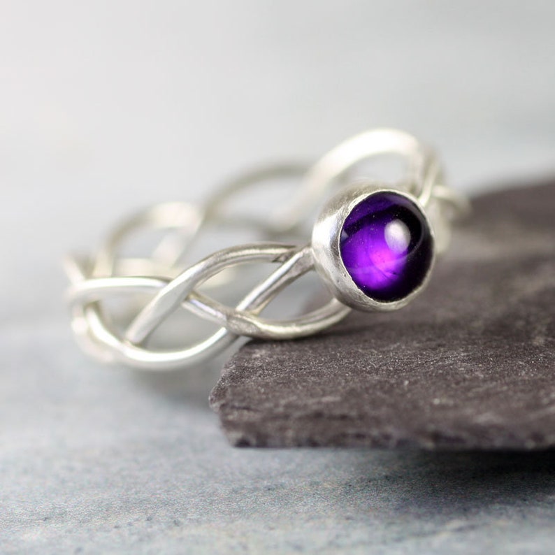 May include: A silver ring with a braided band and a purple amethyst gemstone.