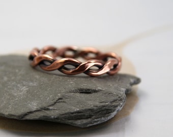 May include: A copper braided ring with a smooth, polished finish. The ring is displayed on a gray stone.