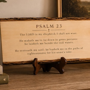 May include: A rectangular light-colored wooden plaque with natural bark edges, featuring the engraved text of Psalm 23. The plaque is supported by a dark brown wooden display stand. The text includes the heading PSALM 23 and verses from the Bible.