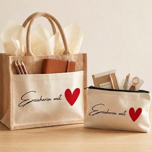 Op de afbeelding: Een beige jute draagtas met een wit canvas voorvak en een bijpassend wit canvas etui. Beide items zijn voorzien van de zwarte tekst "Erzieherin mit" en een rood hartje. De tas bevat potloden en een bruin notitieboekje.