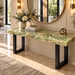Può includere: Un tavolo console rettangolare con un piano in pietra onice verde lucidata, caratterizzato da venature naturali e una finitura liscia. Il tavolo è sostenuto da due robuste gambe in metallo nero opaco a forma di U con vasi e libri sopra.